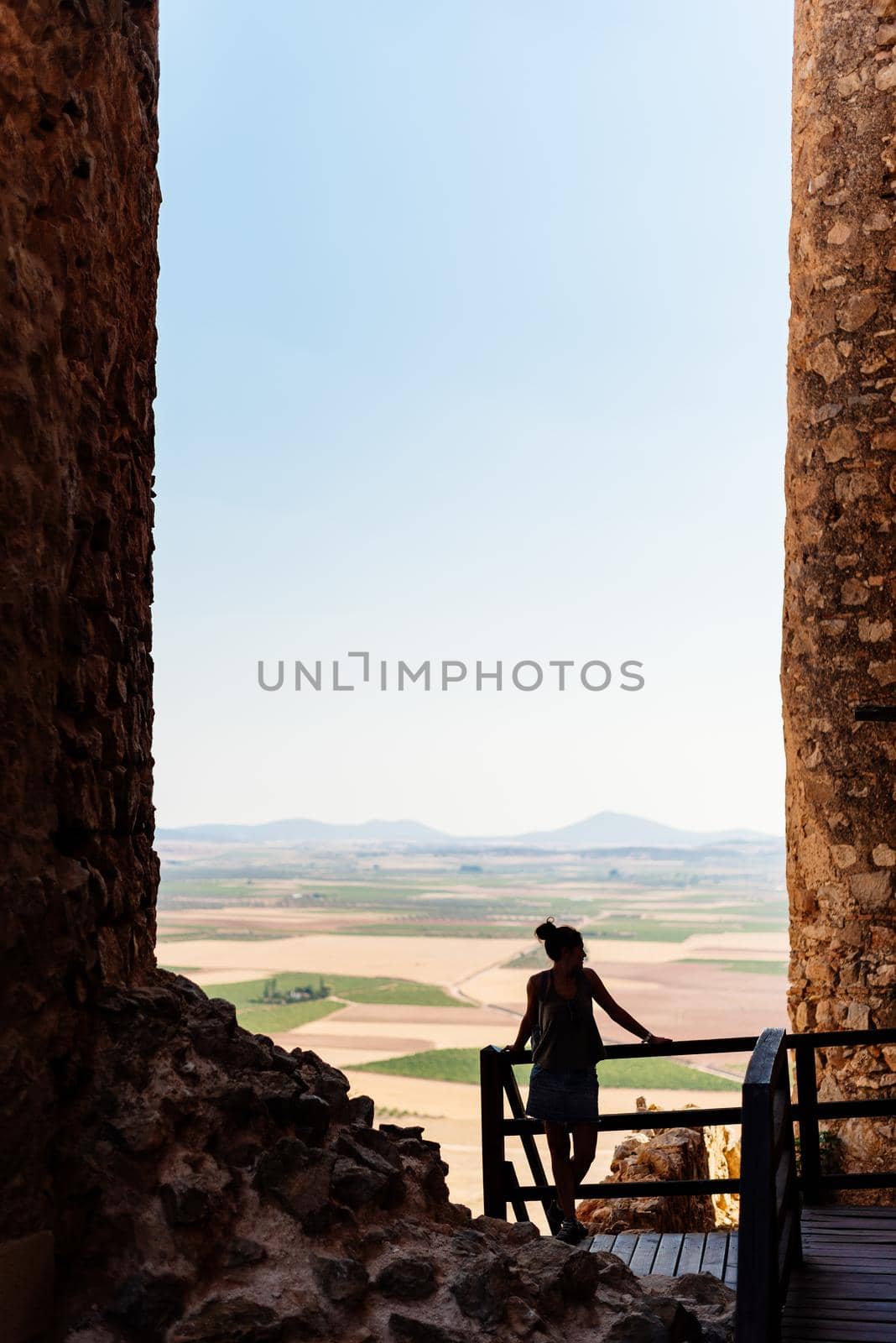 Vertical photo of a woman leaning on a railing between the towers of historic windmills on a hill in Toledo, Spain.