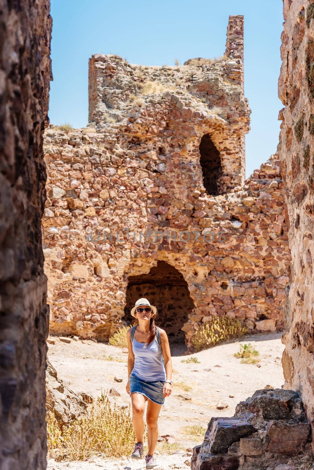 Vertical photo of a woman with summer clothes, a hat and sunglasses visiting a restored stone castle in a sunny day