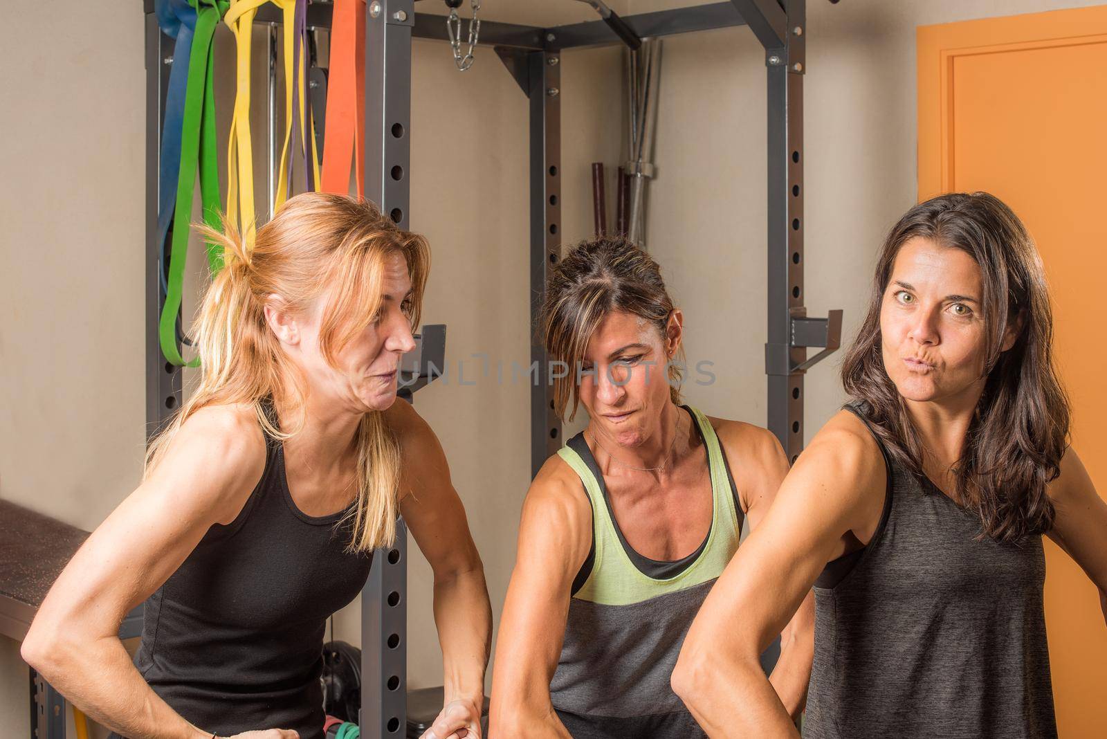 Portrait of three sportswoman showing arms muscles in funny way in gym by ivanmoreno