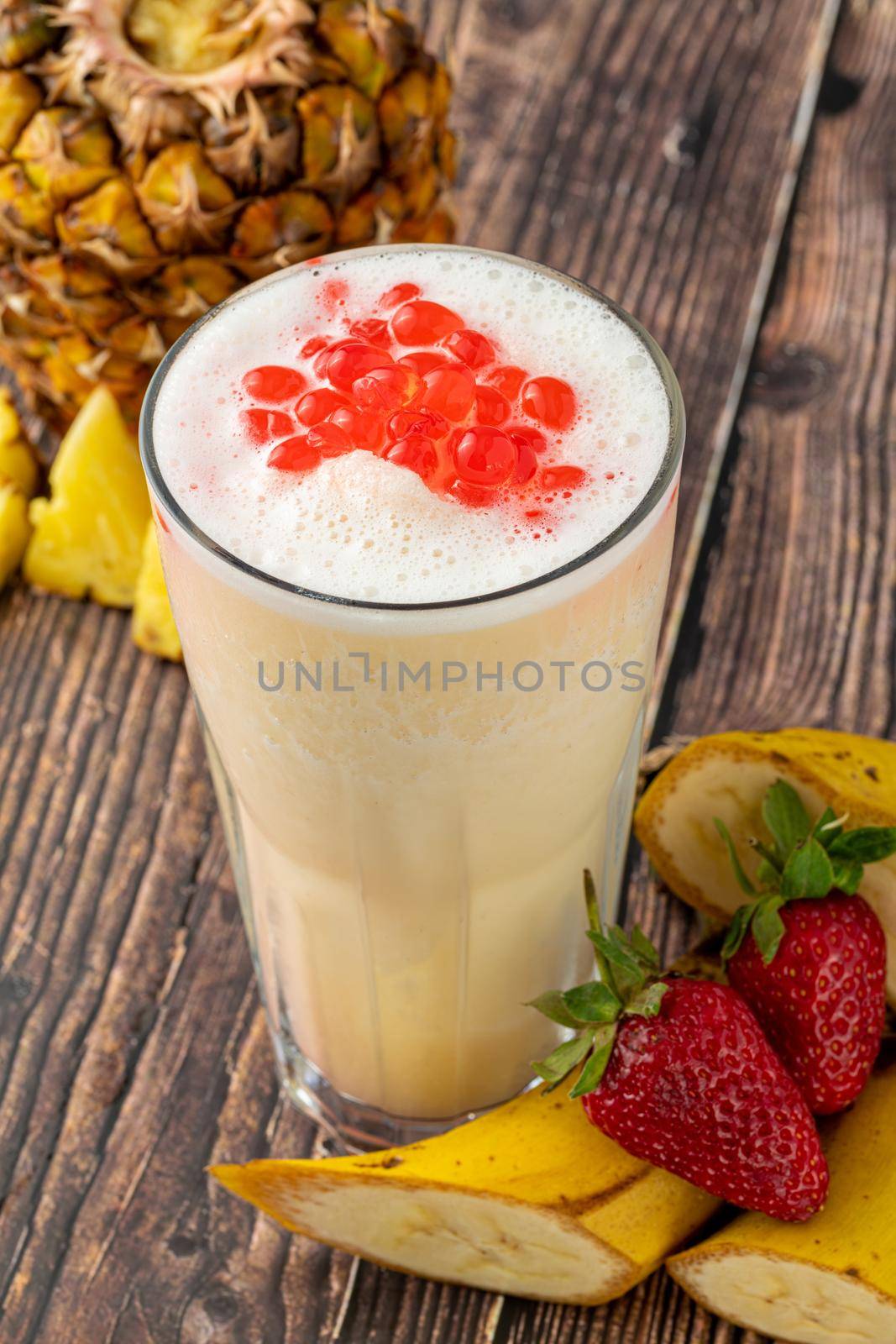 Banana, strawberry and pineapple smoothie on wooden table and bubble tea or boba tea balls on it by Sonat