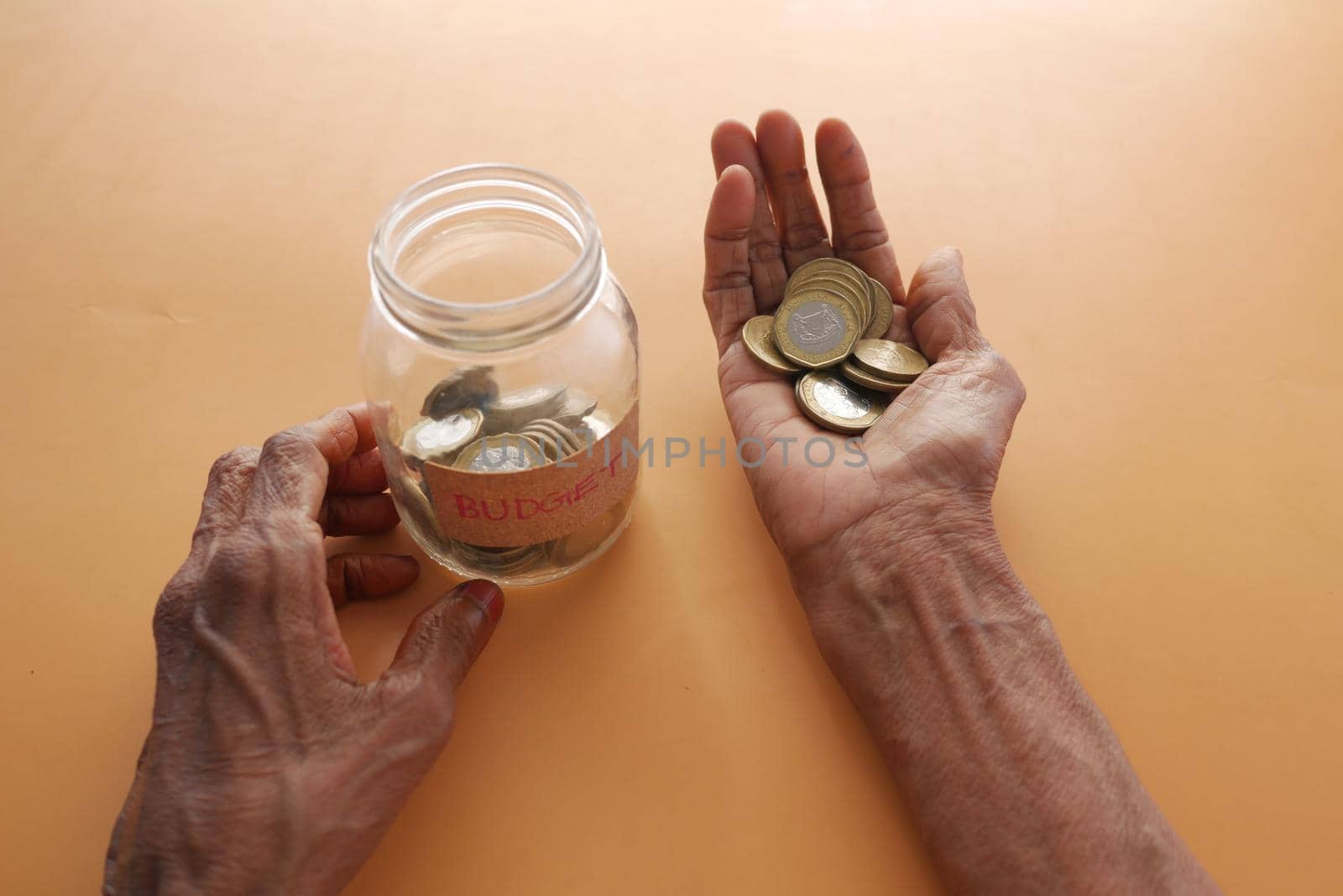 Close up of senior women hand saving coins in a jar ,