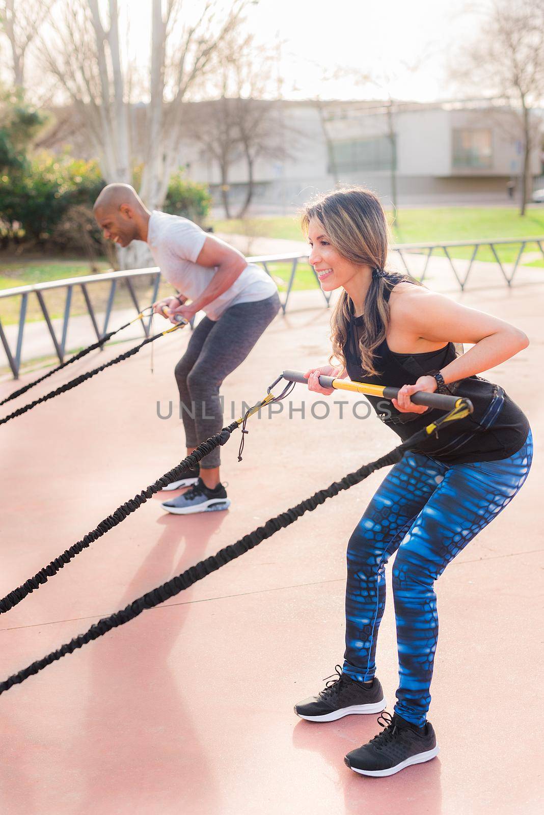 Fitness people exercising arms with an elastic gym stick in the park. Multi-ethnic people exercising outside.