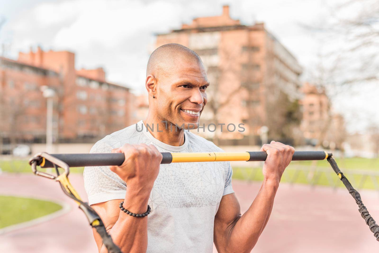 Atlhetic latin sportsman exercising with an elastic gym stick in the park. Hispanic adult man exercising outside.