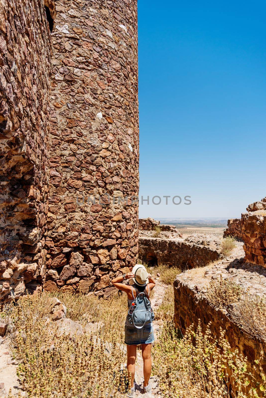 Woman taking his hat and standing in front of the defense stone walls of a medieval castle. Almonacid Castle, Toledo