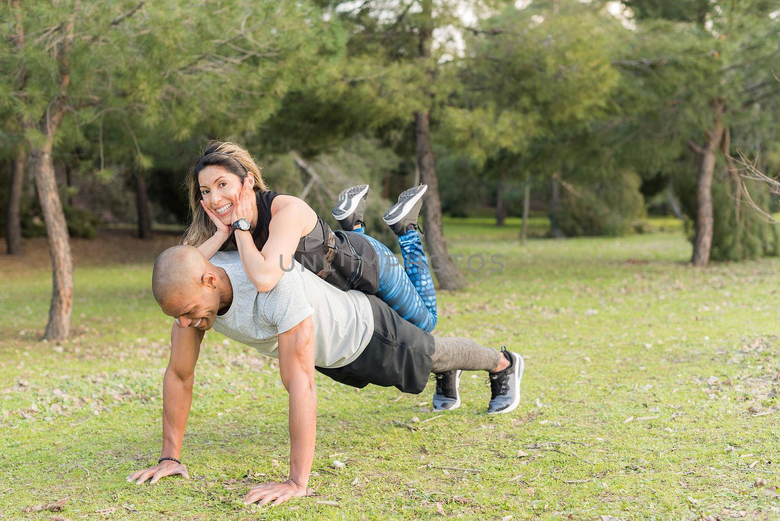 Fitness couple doing push-ups in the park. Multi-ethnic people exercising outdoors.