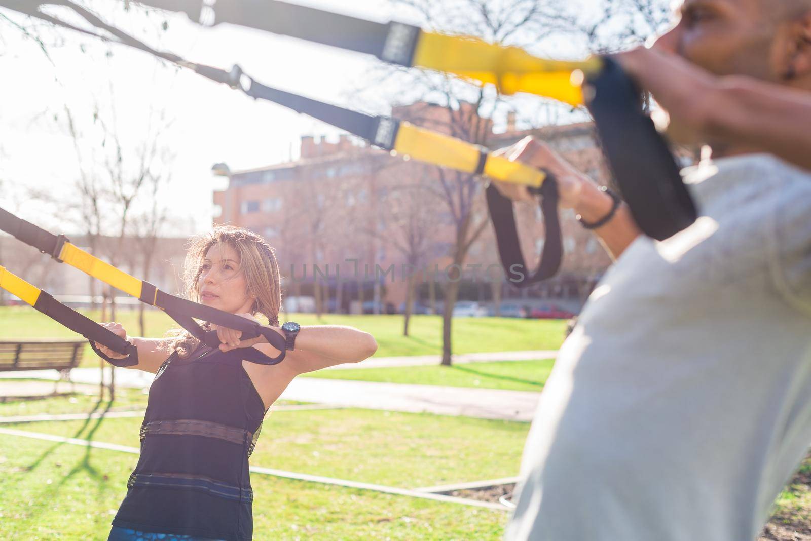 Fitness couple exercising with trx fitness straps in the park. Adult man and woman exercising outdoors.