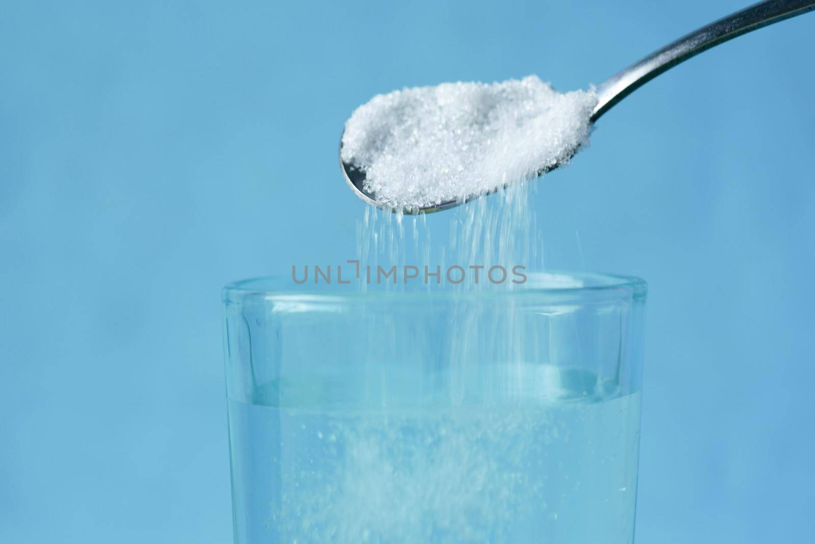 pouring white sugar in a glass of water on table ,