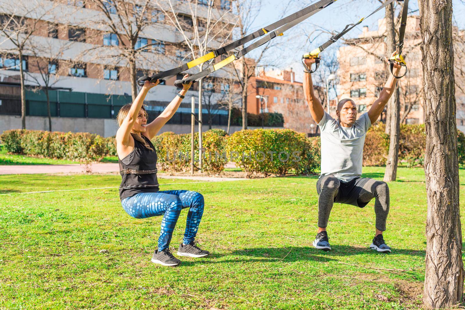 Couple of athletes exercising with trx fitness straps in the park. Adult man and woman exercising outdoors.