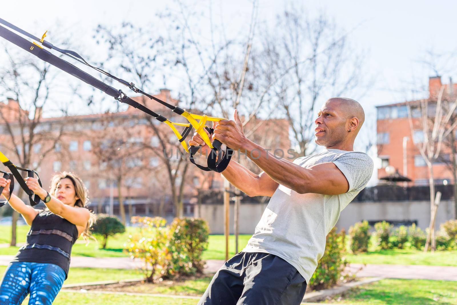 Fitness couple doing arms and biceps exercise with trx fitness straps in park. Focus on sportsman. by ivanmoreno