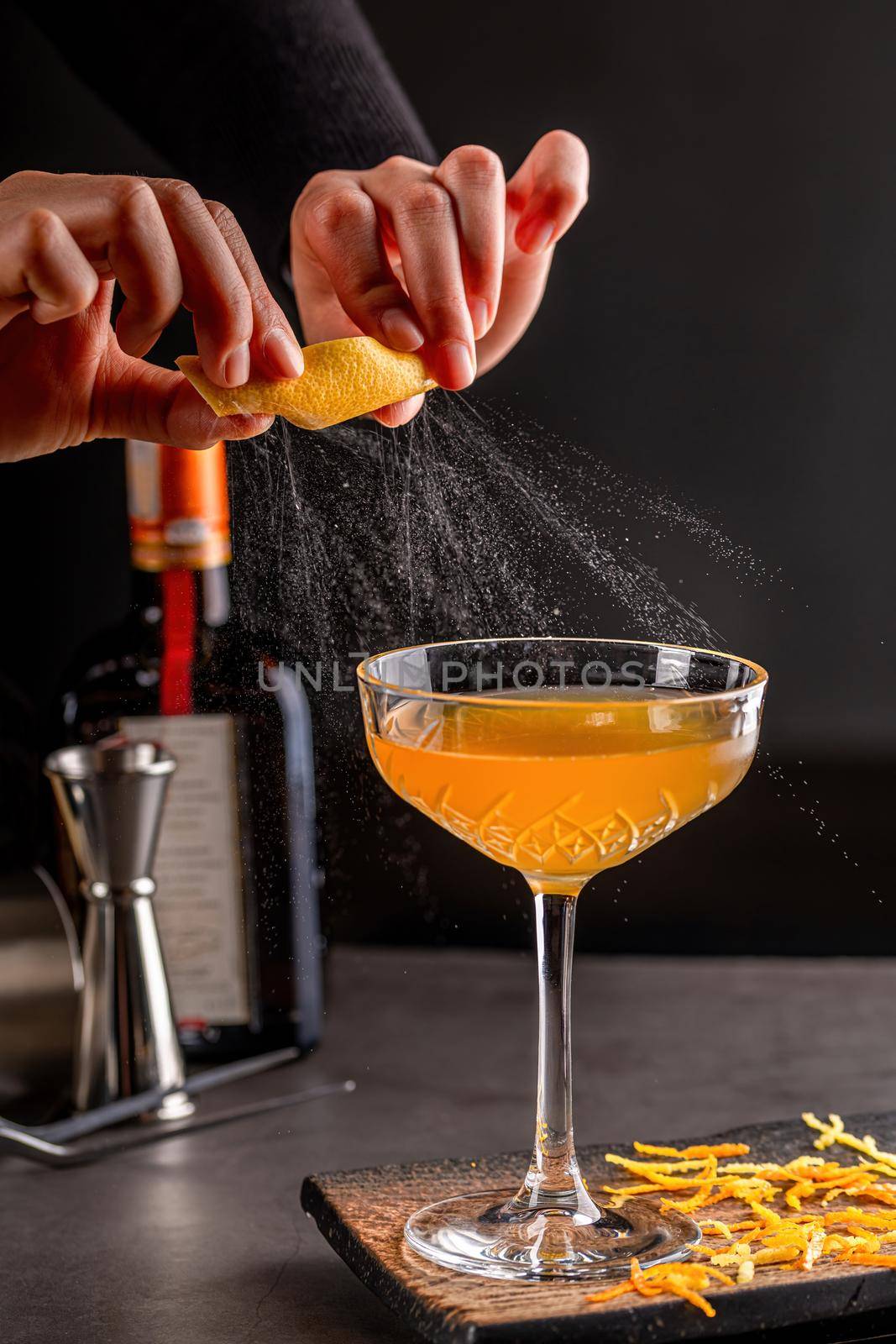 Professional female bartender flavoring a luxury cocktail with impressively spray from citrus peel. Cocktail zest shoot by Sonat