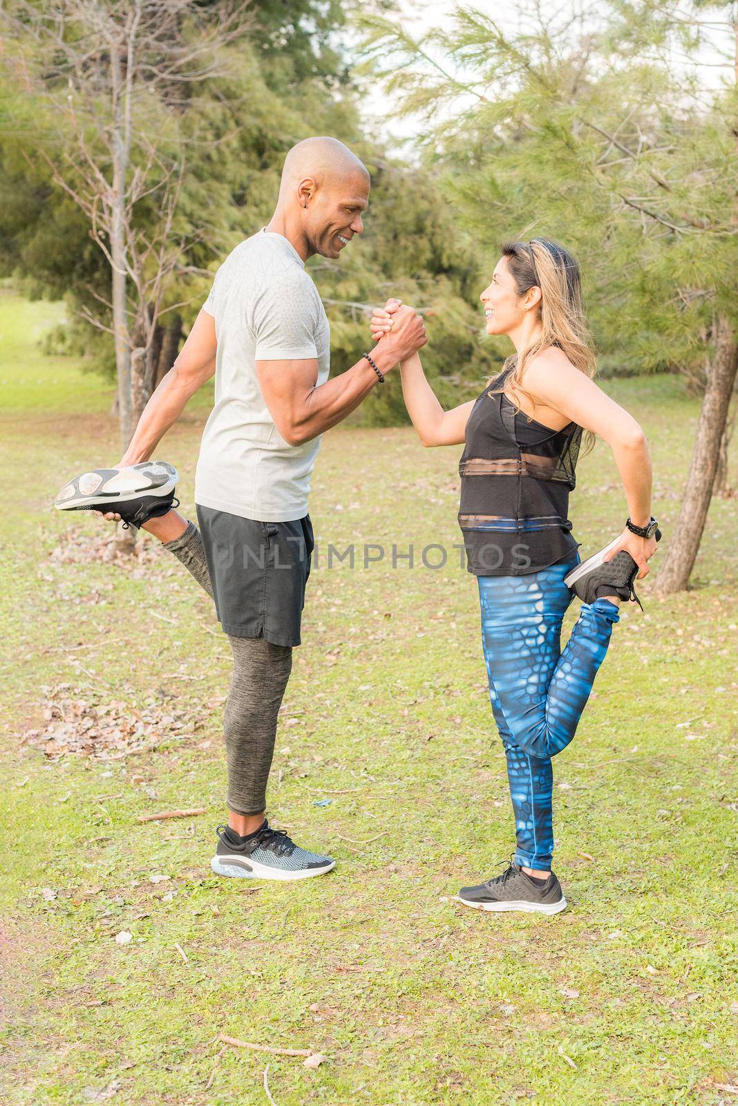 Fitness couple exercising by holding with one hand in the park. Multi-ethnic people exercising outside.