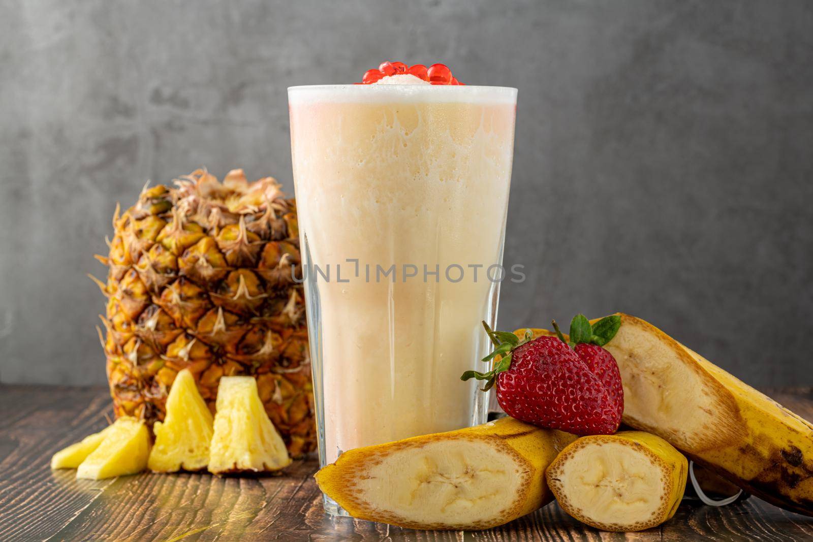 Banana, strawberry and pineapple smoothie on wooden table and bubble tea or boba tea balls on it by Sonat