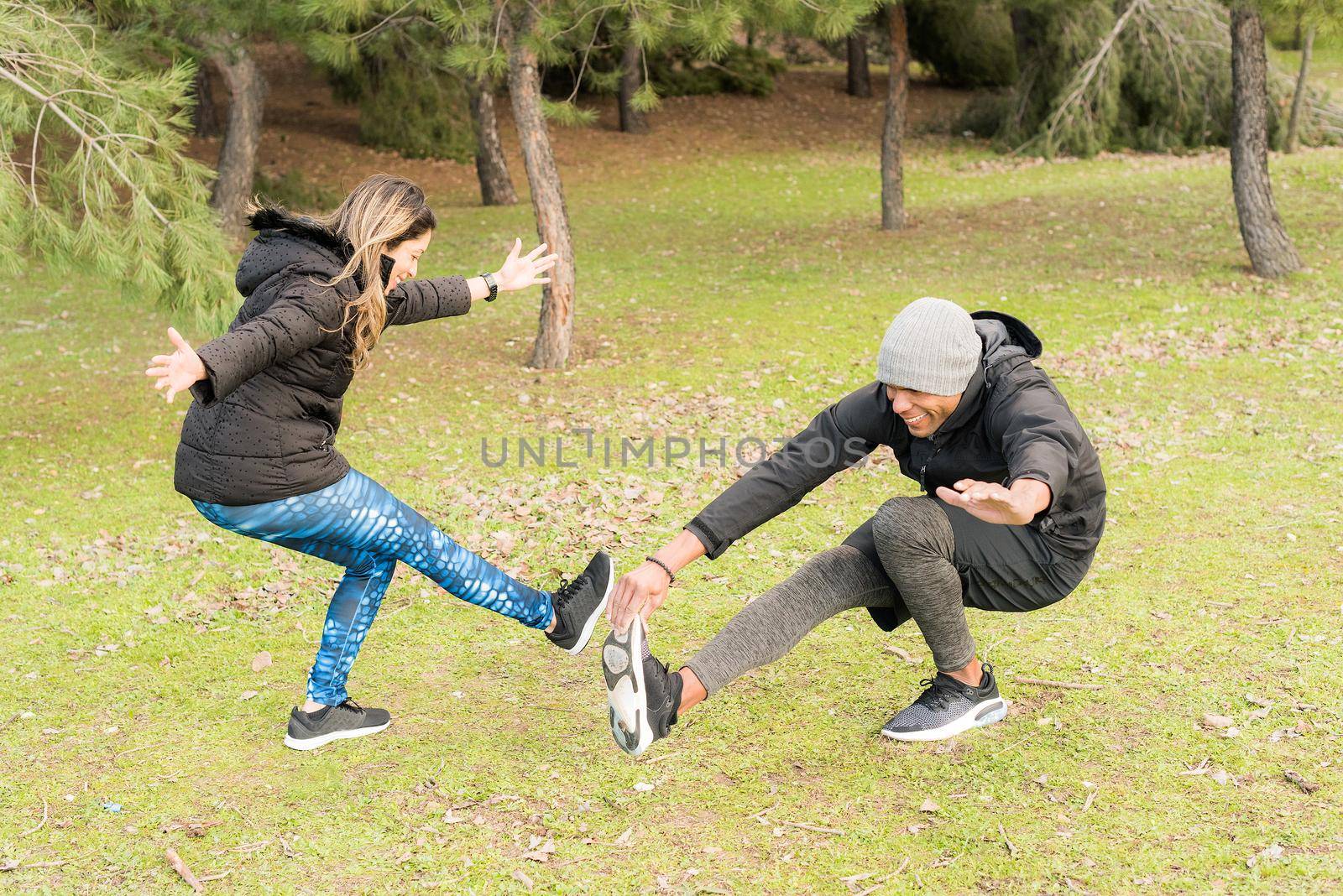 Fitness couple in warm clothes standing on one leg and stretching the other. Multi-ethnic couple outdoors.