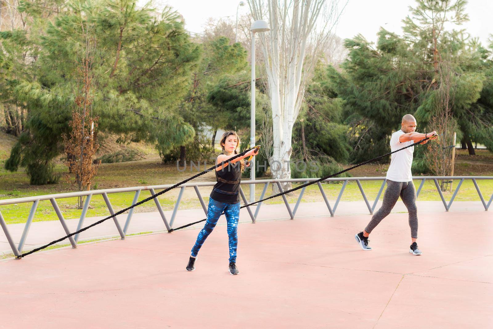 Fitness couple exercising with an elastic gym stick in the park. Multi-ethnic people exercising outside.