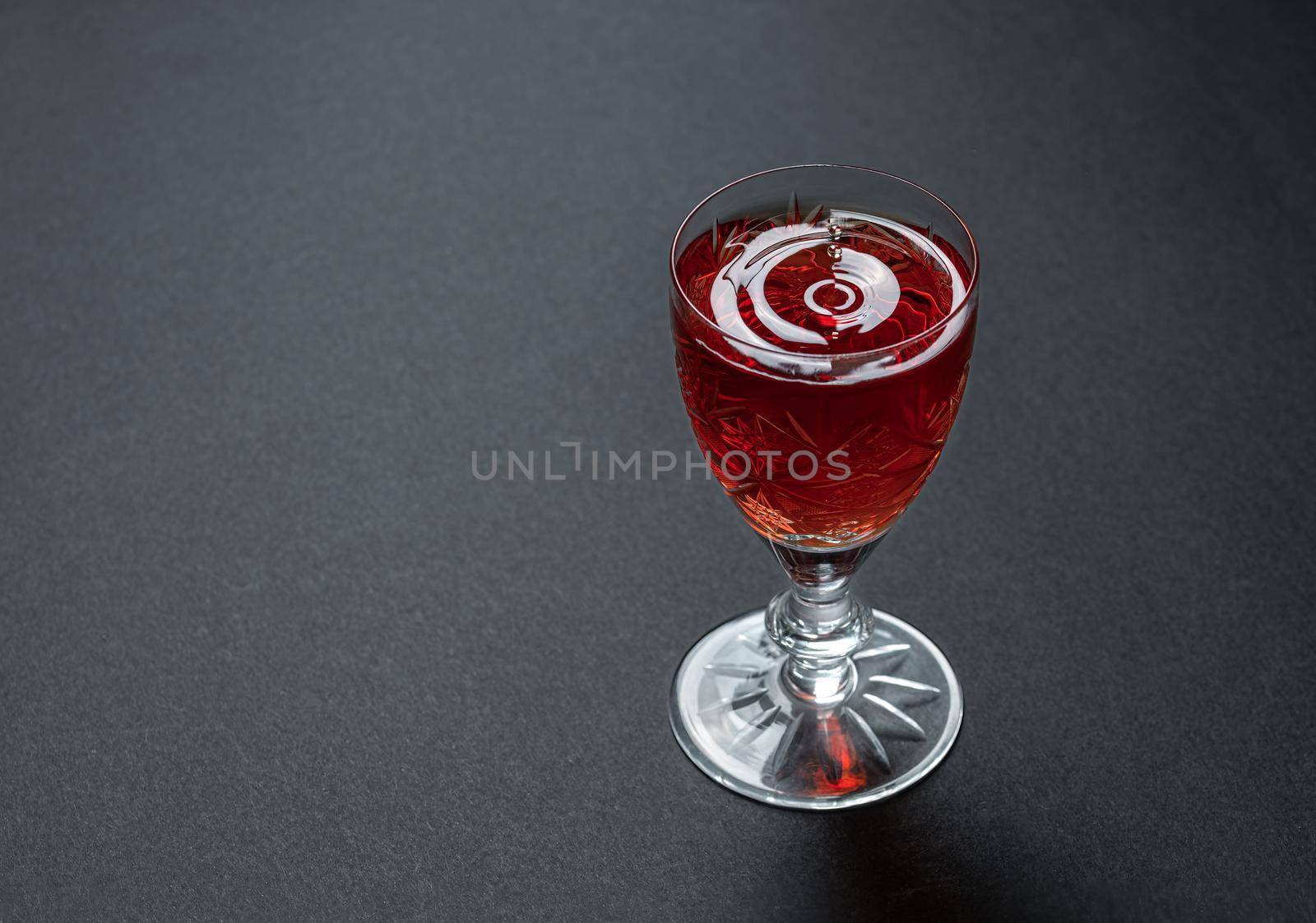 Luxurious cocktail in a crystal goblet with waves of drops on a dark stone background