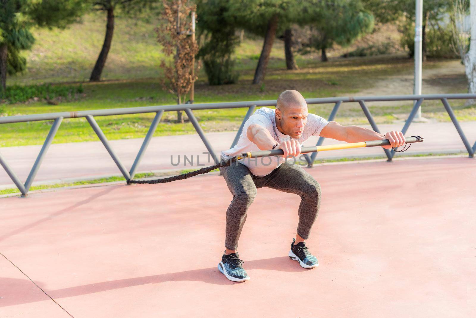 Sportsman exercising with an elastic gym stick in the park. Latino man exercising outside.