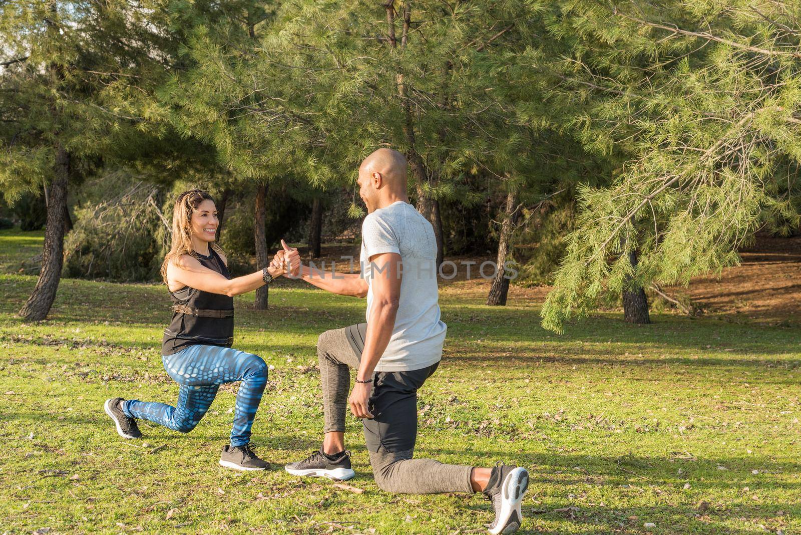 Fitness couple exercising by holding hands in the park. Multi-ethnic people exercising outside.