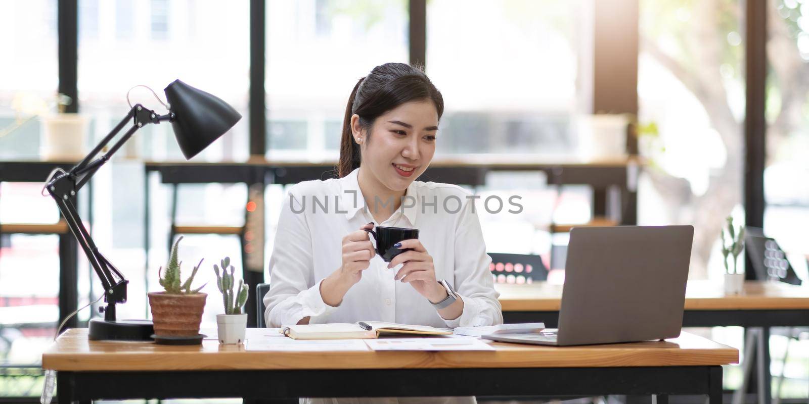 Young asian businesswoman have the pleasure of watching work on laptop tablet and favorite coffee at the office. by wichayada
