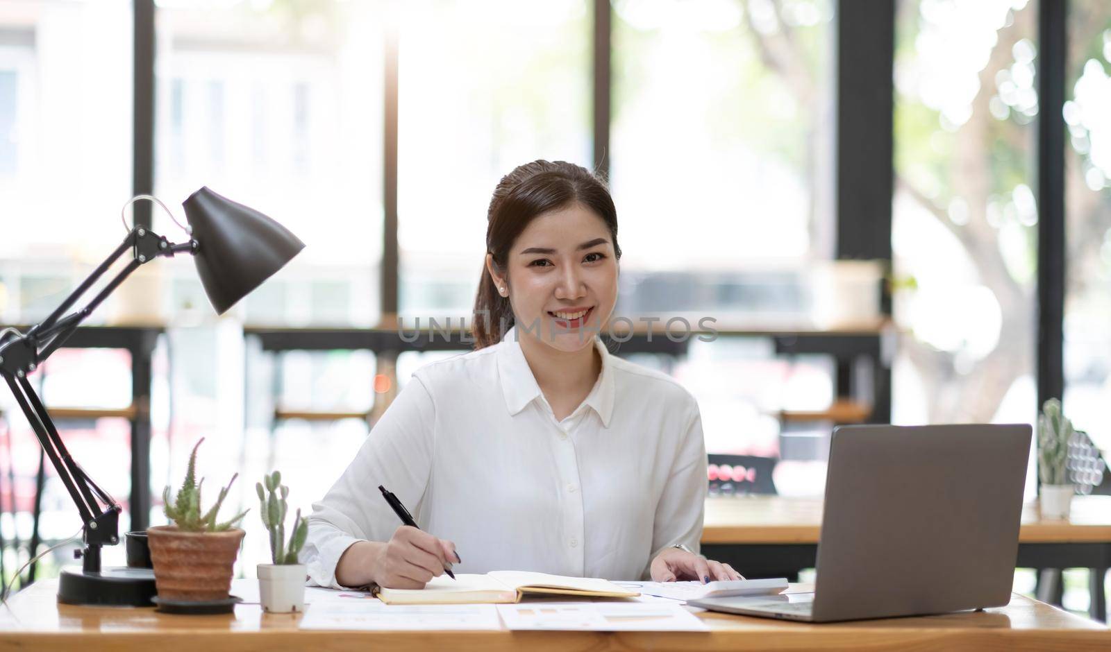 Charming Asian businesswoman working with a laptop at the office. Looking at camera. by wichayada