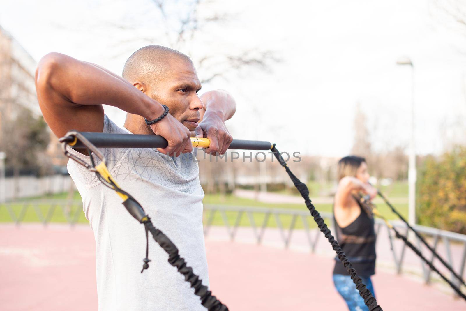 Atlhetic multi-ethnic people exercising arms with an elastic gym stick in the park. Focus on sportsman by ivanmoreno