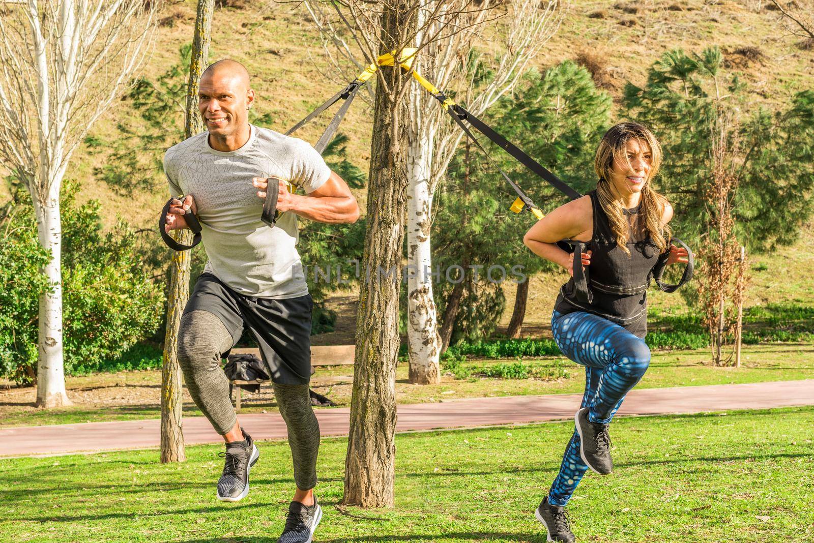 Fitness couple doing back legs exercise with trx fitness straps in park by ivanmoreno