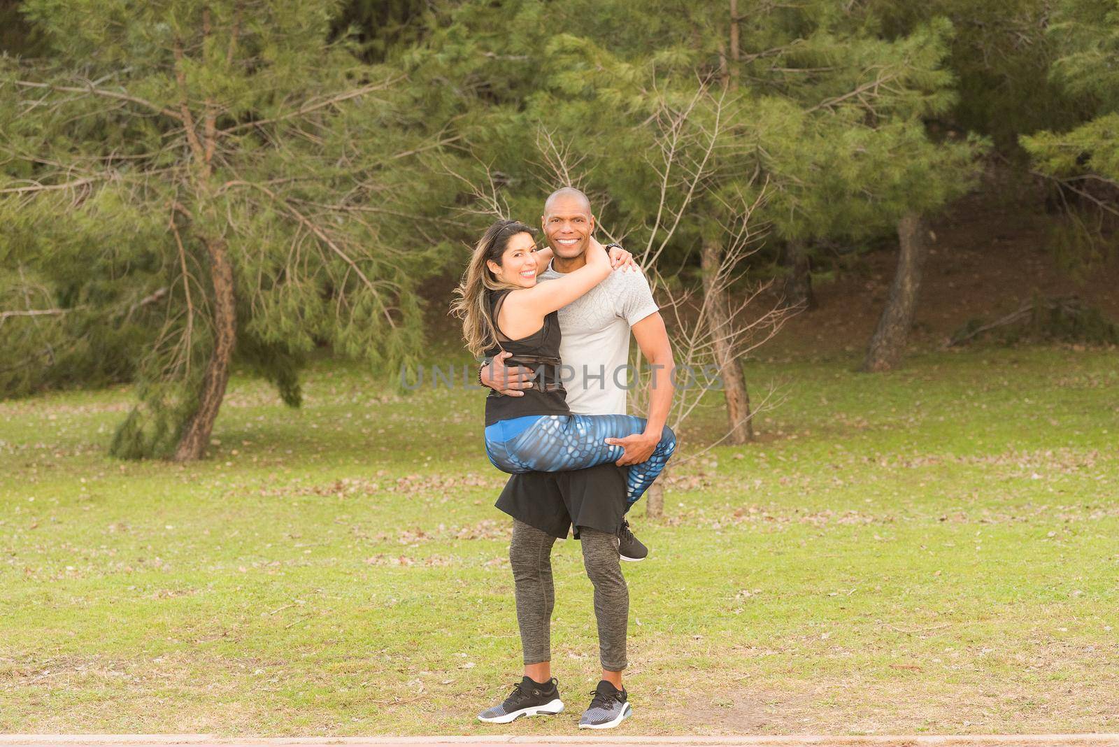 Fitness couple hugging looking at the camera in the park. Multi-ethnic couple exercising outdoors.