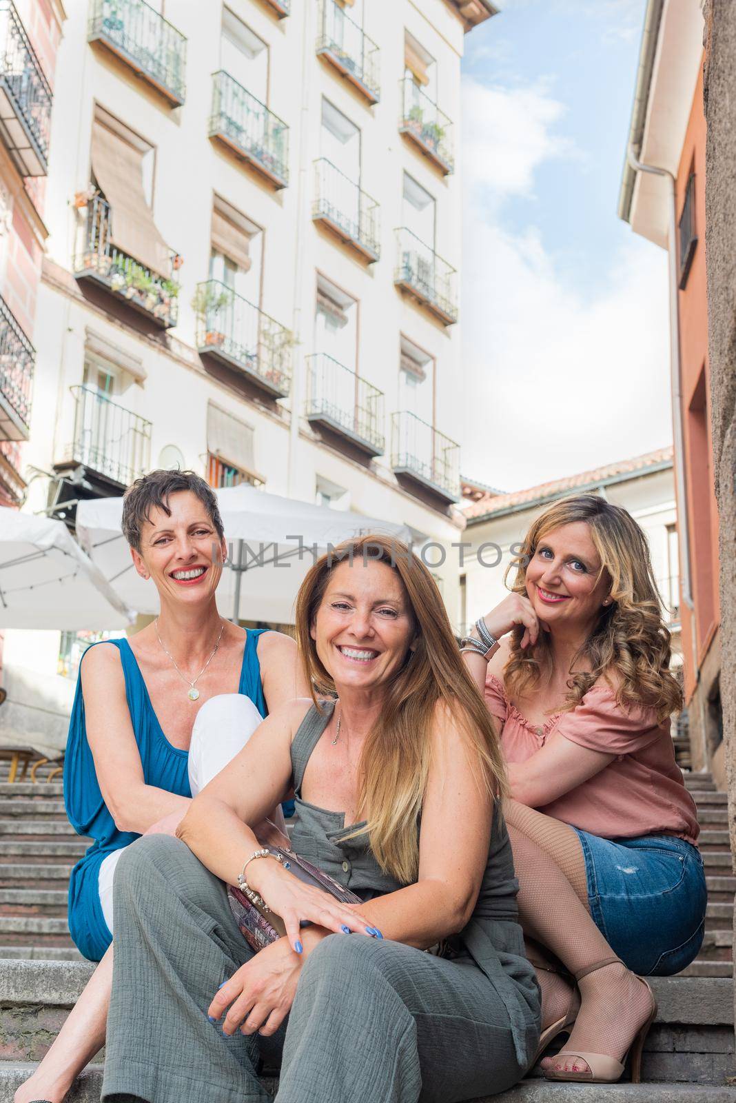 Three cheerful adult women sitting in stoned stairs and looking at the camera. Beautiful mature women having a good time together.