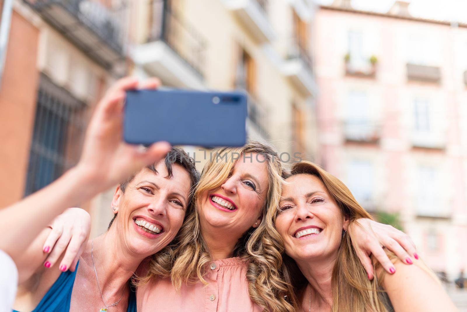 Three mature female friends hugging together taking a selfie. Middle aged friends sharing time together and having fun.