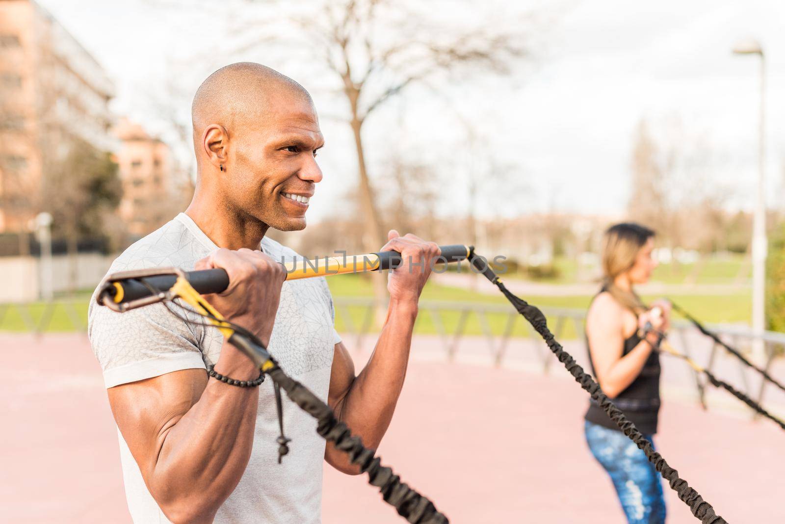 Athletic people exercising with an elastic gym stick in the park. Focus on sportsman. Multi-ethnic people exercising outside.