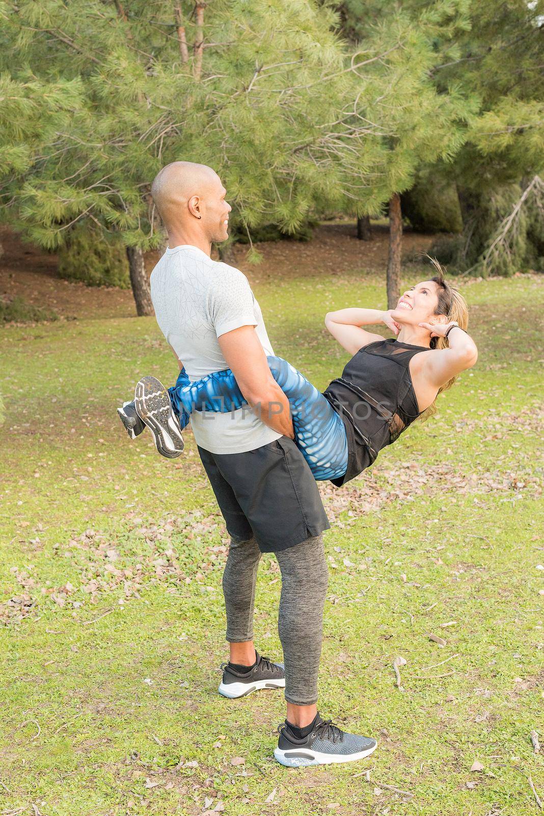 Fitness couple doing abdominal excersise while he holding she for her legs. Couple doing exercise outdoors together.