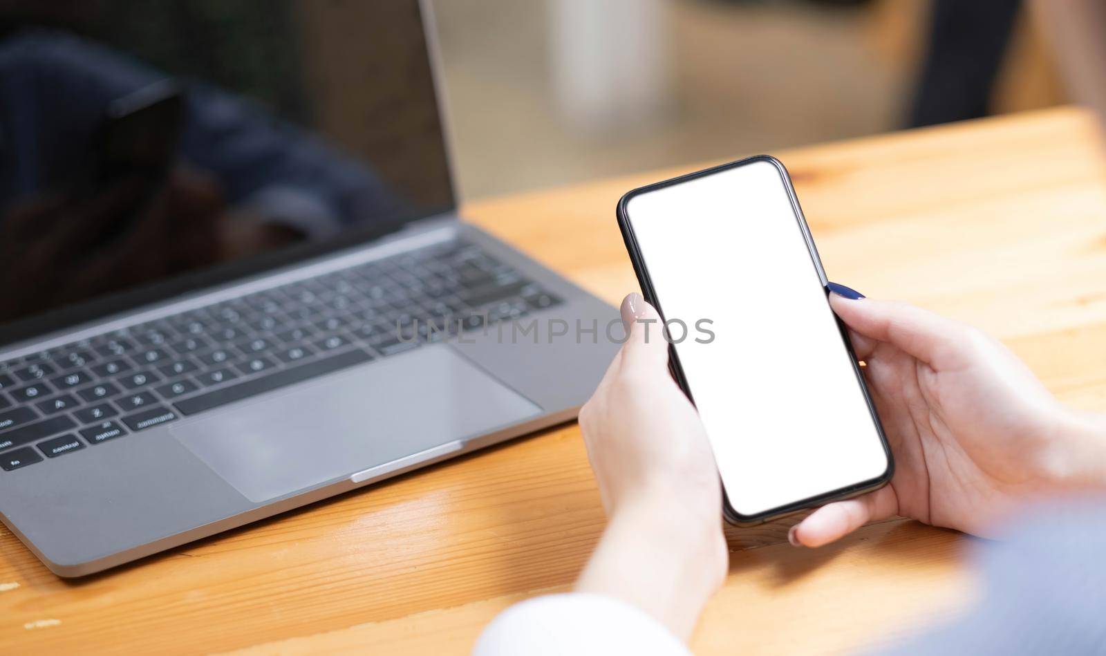 hand woman using a telephone, empty screen smart phone and computer on wooden table top view. by wichayada