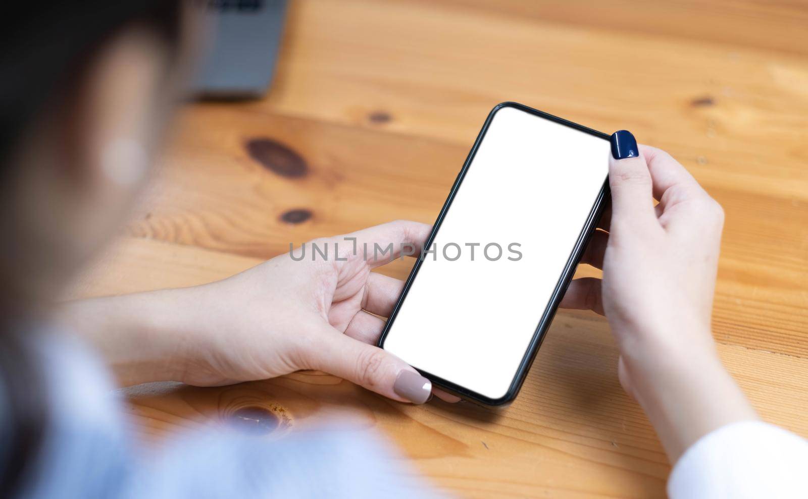 hand woman using a telephone, empty screen smart phone and computer on wooden table top view. by wichayada