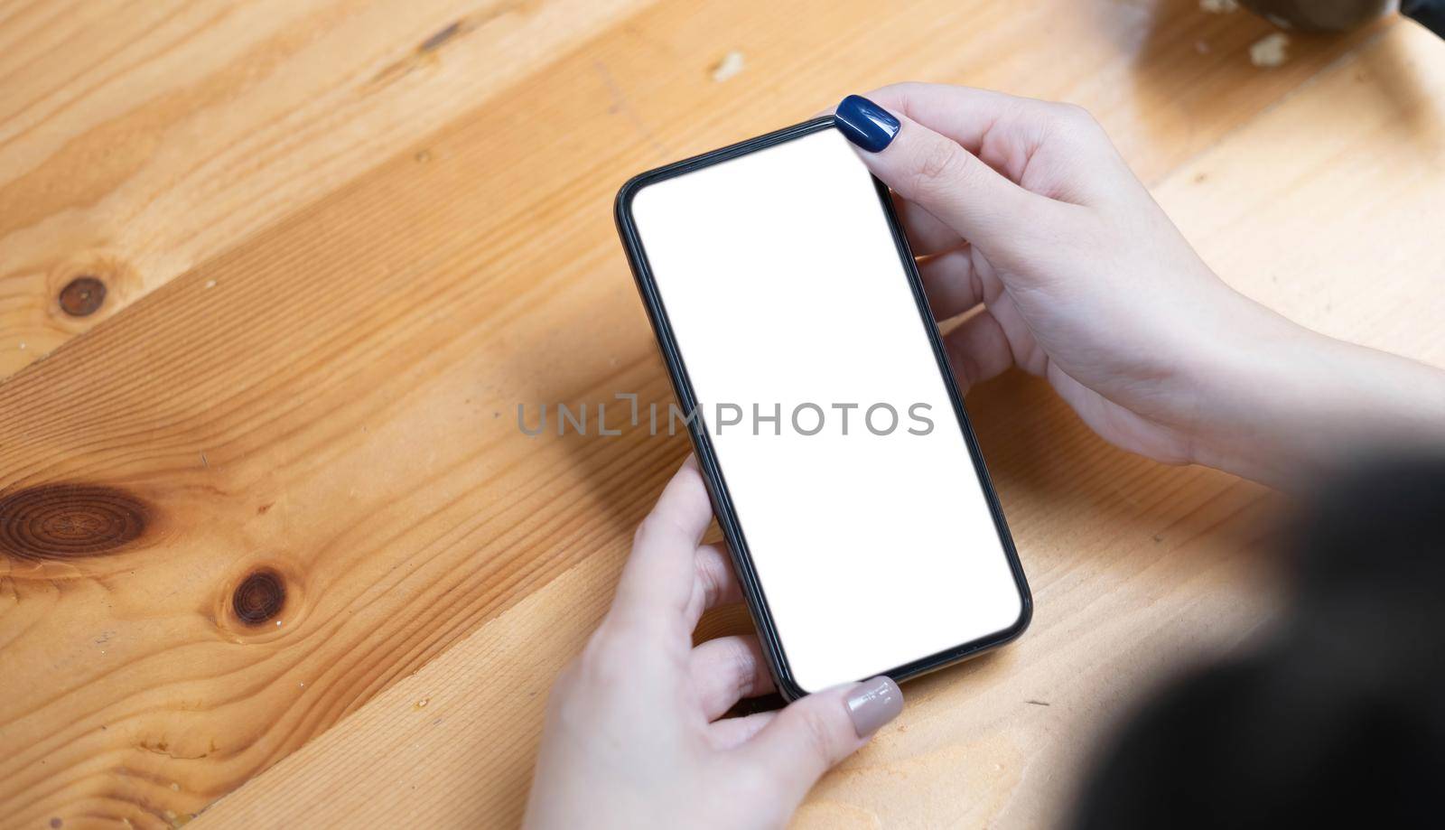 hand woman using a telephone, empty screen smart phone and computer on wooden table top view. by wichayada