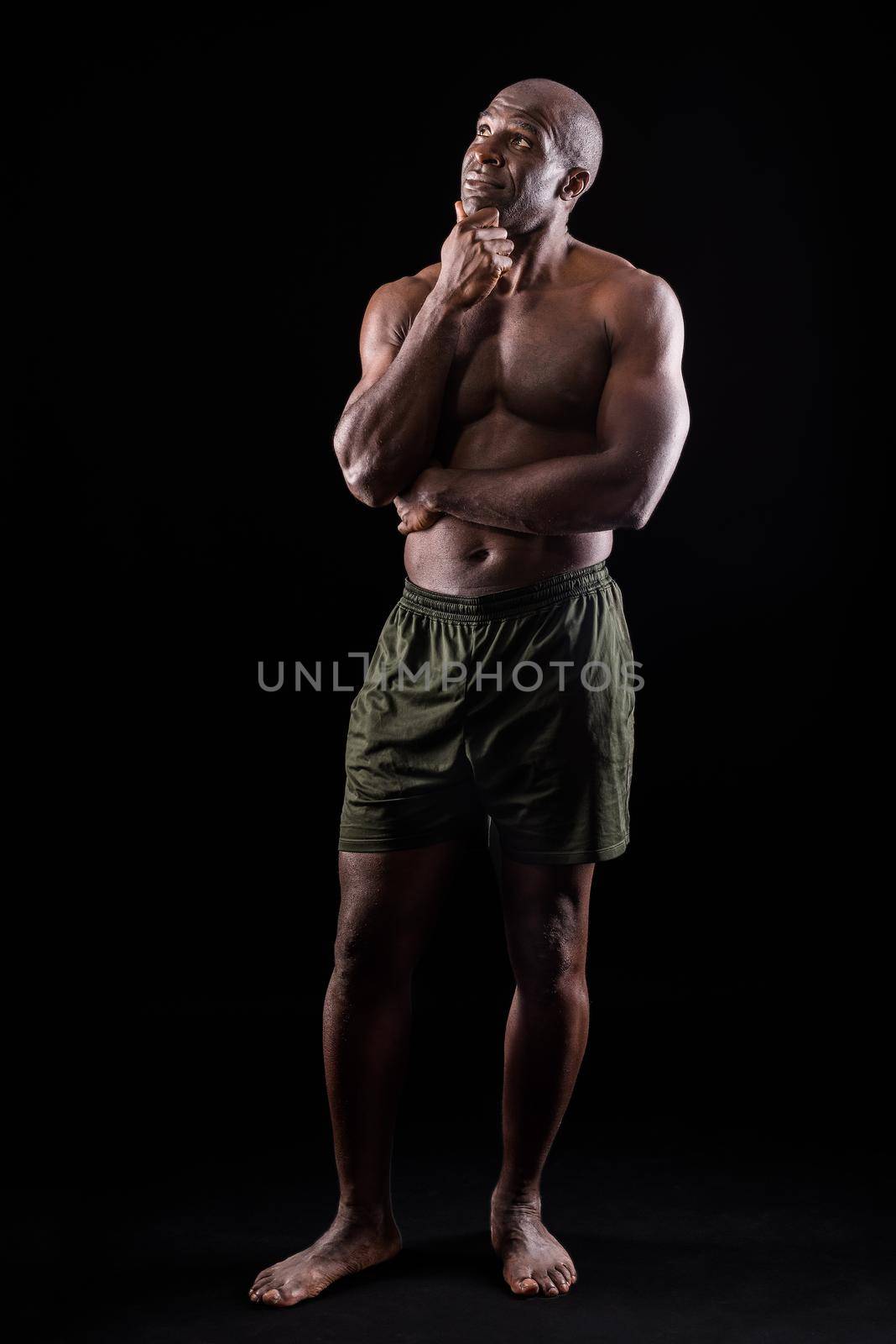 Adult African American in shorts standing with thoughtful expression. Muscular adult male with naked torso with hand on knob with thinking expression.