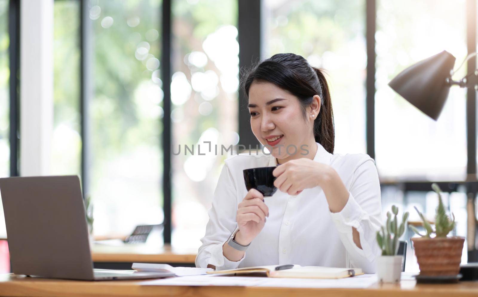 Young asian businesswoman have the pleasure of watching work on their laptop and favorite coffee at the office. by wichayada