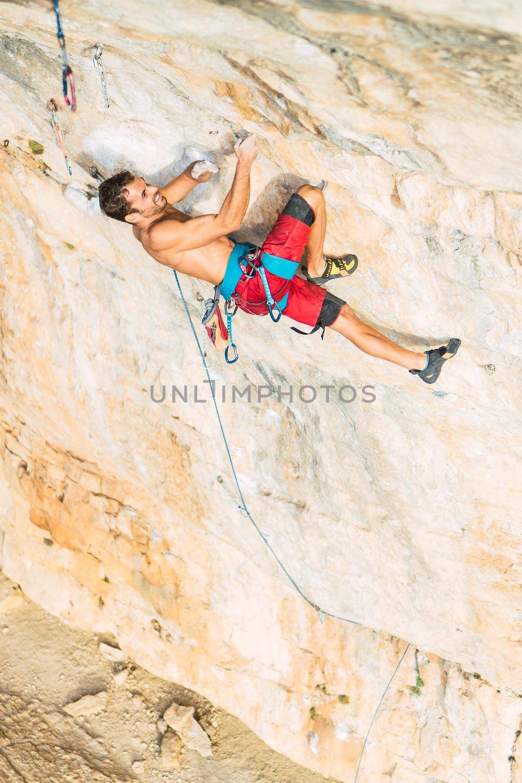 Aerial view of a rock climber holding on with both hands and feet on rock. Climber with bare torso making an effort to climb the rock.