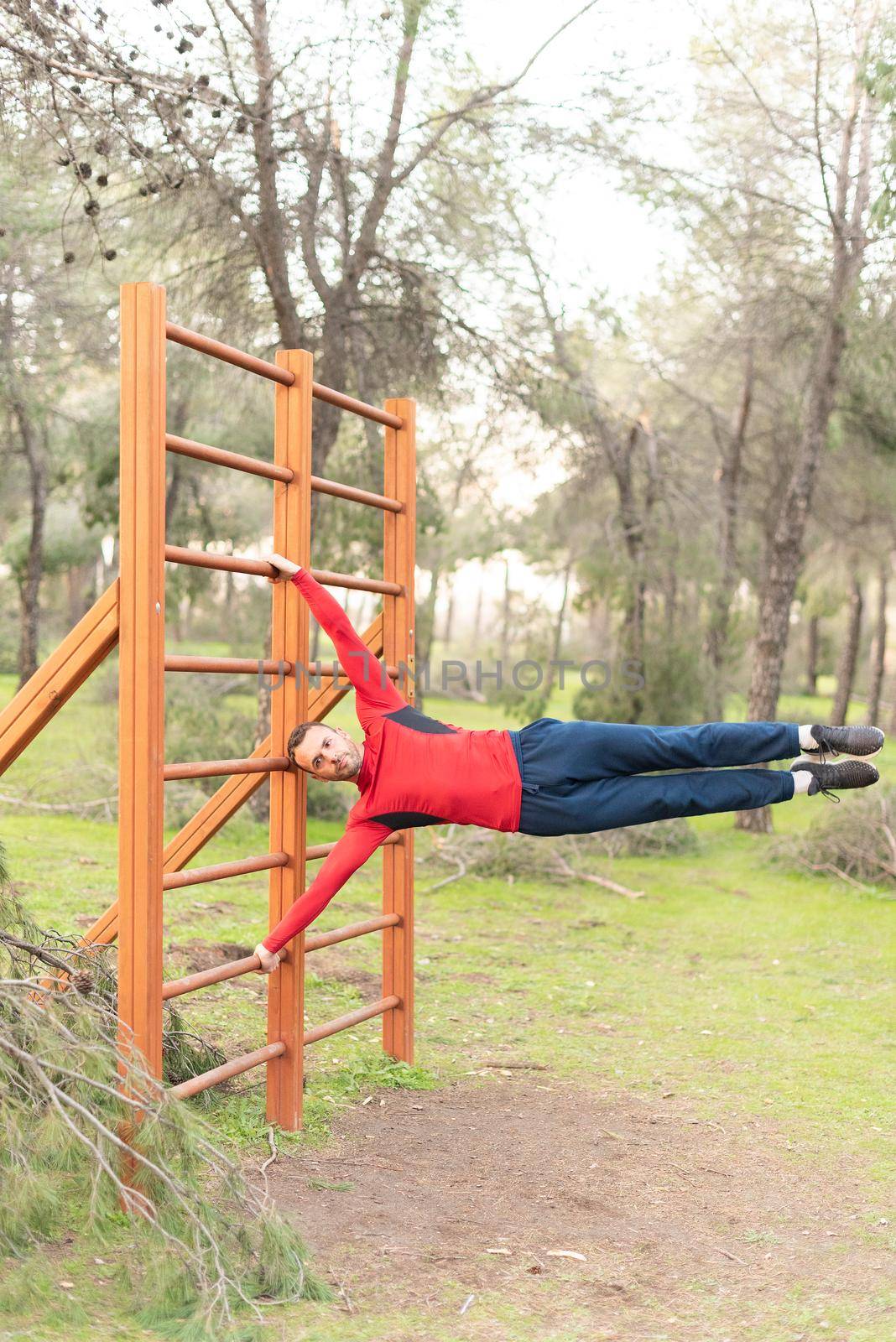 Young man doing exercises on vertical bar in park. Gymnastic man performing human flag figure on bars in a park.