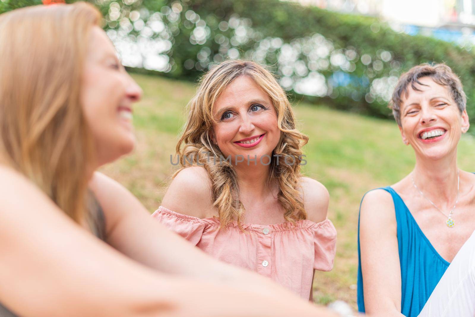 Close up view of three adult women sitting in the park laughing . Beautiful mature women having a good time together in the park.