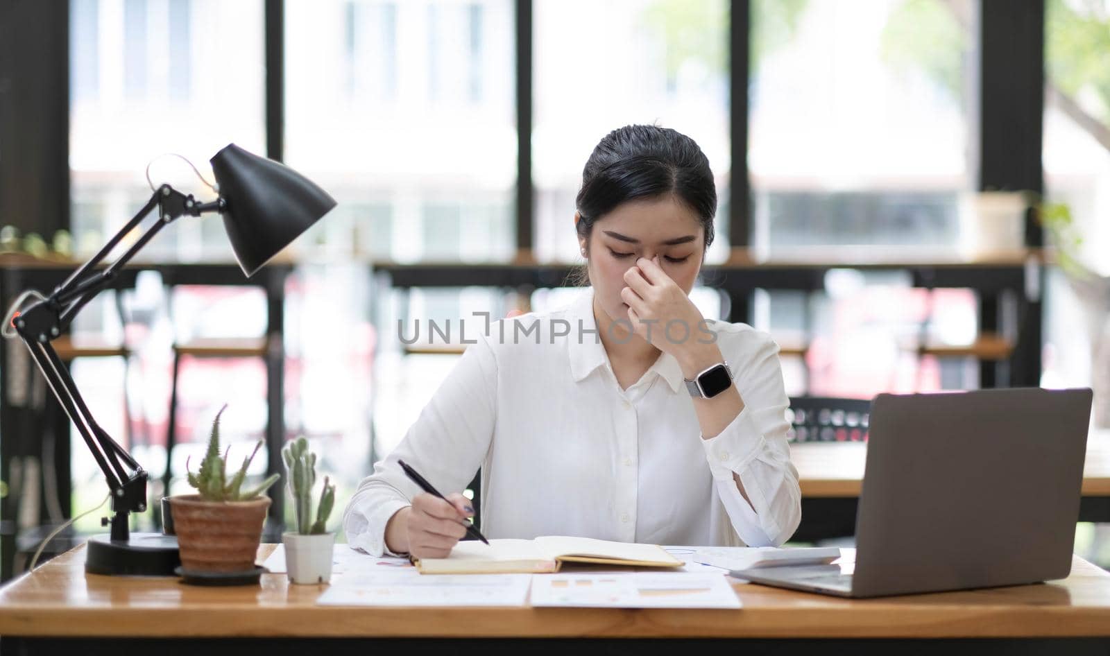 Young Asian woman feeling migraine head strain. Tired, Overworked businesswoman financier while working on laptop computer in office..