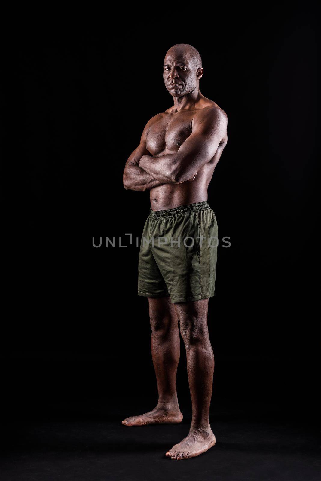 Adult African American in shorts standing with arms crossed looking at camera seriously on a black background by ivanmoreno