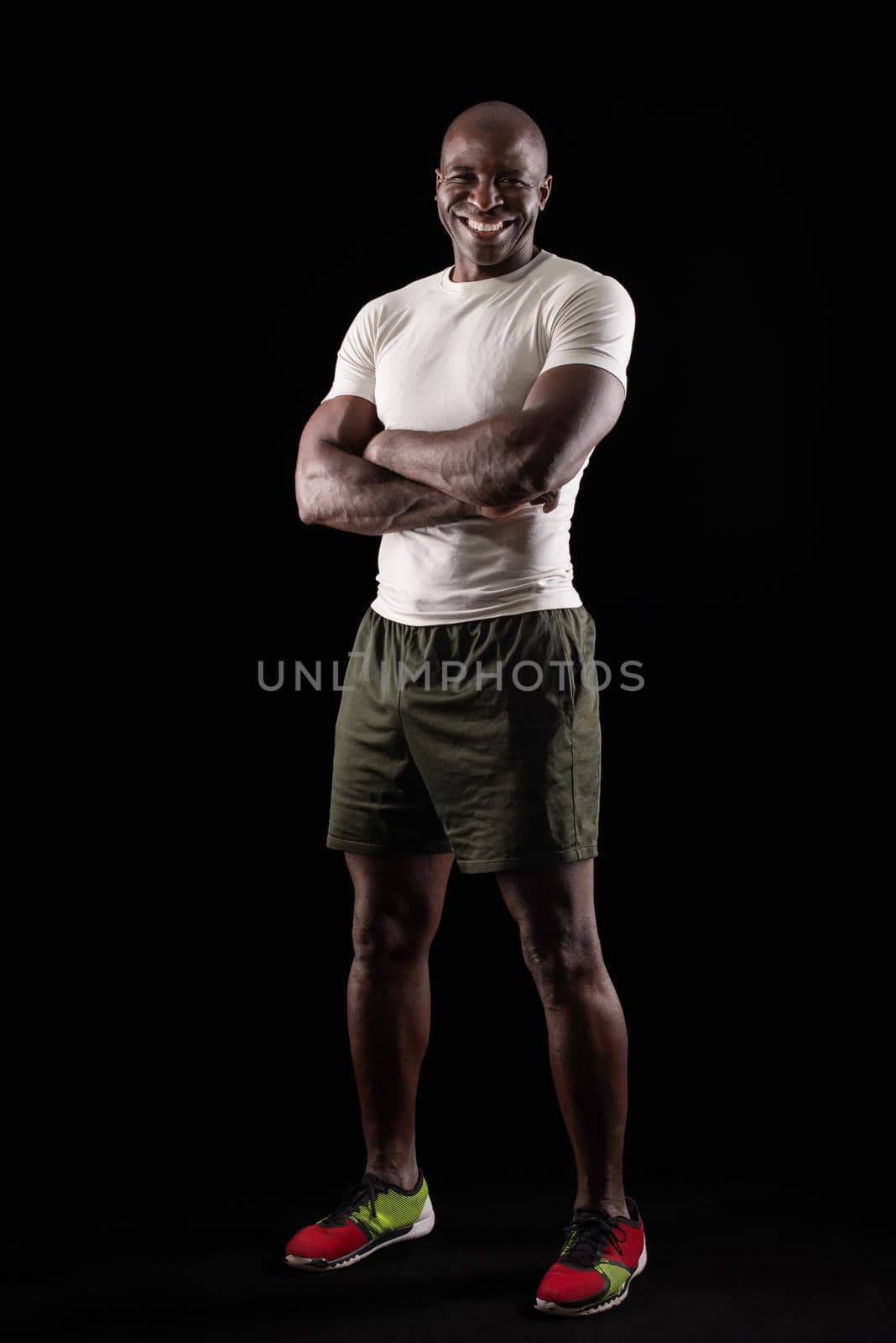 Portrait of african american adult man wearing sportswear posing with crossed arms on a black background. Muscular adult man standing looking at camera in studio.