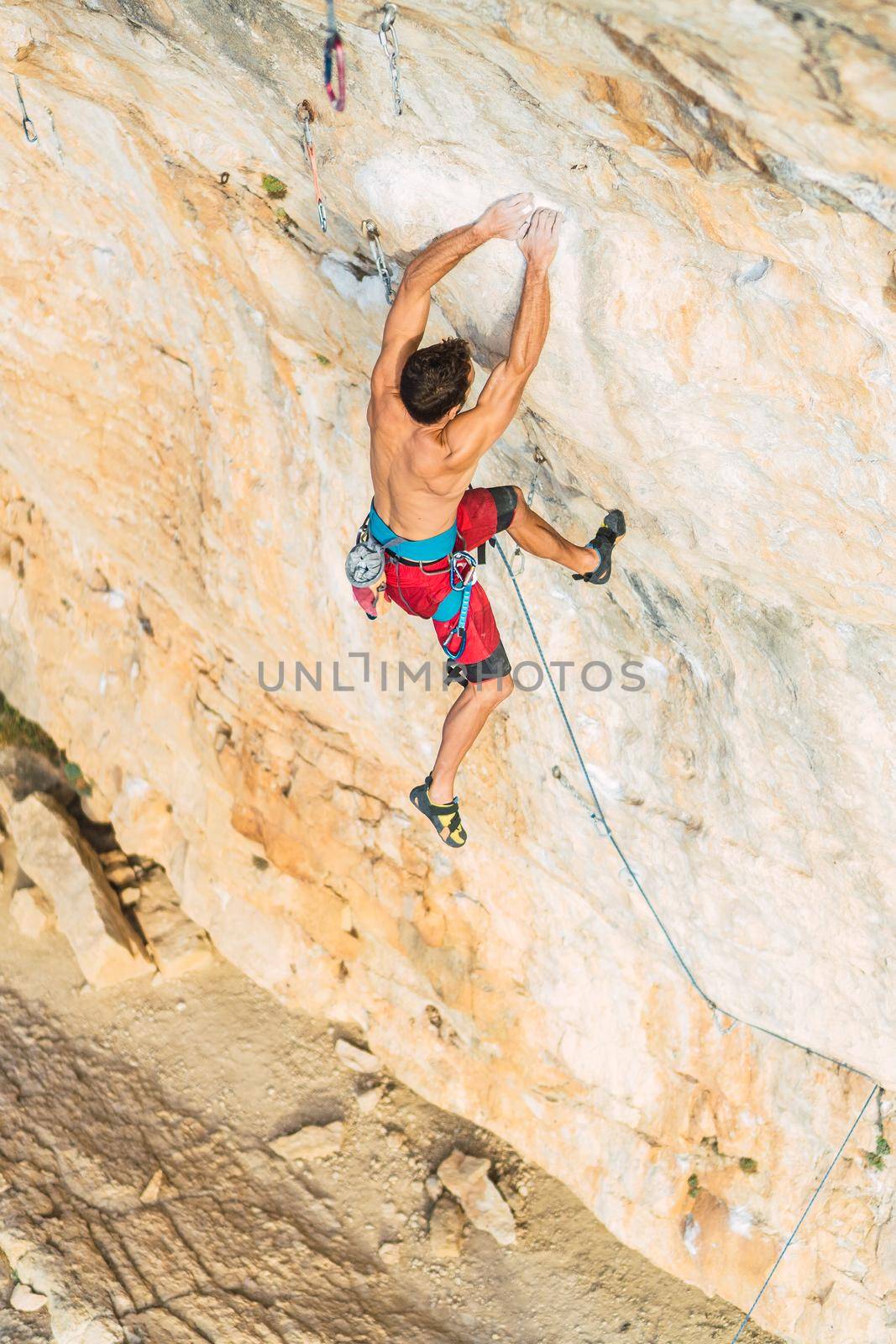 Aerial view from above of the back of a man climbing a rock formation. Man with bare torso climbing a rock wall.