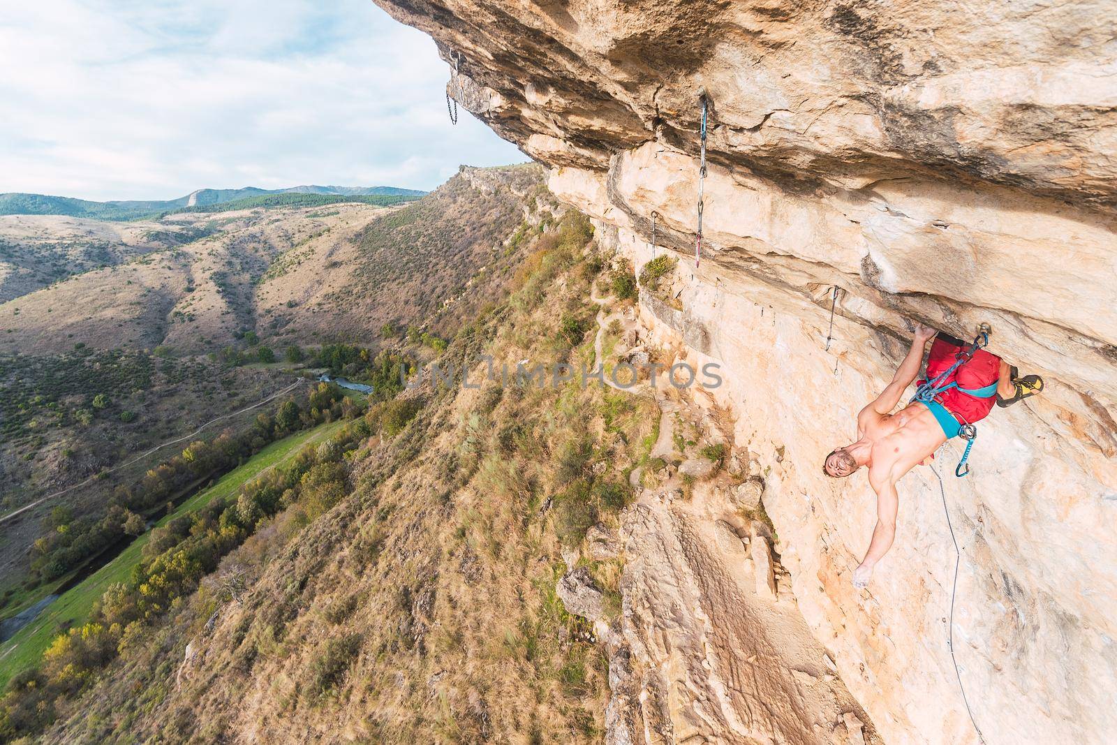 Young male climber hanging from a rock with his body facing outward. Climber with bared torso climbing on a mountain.