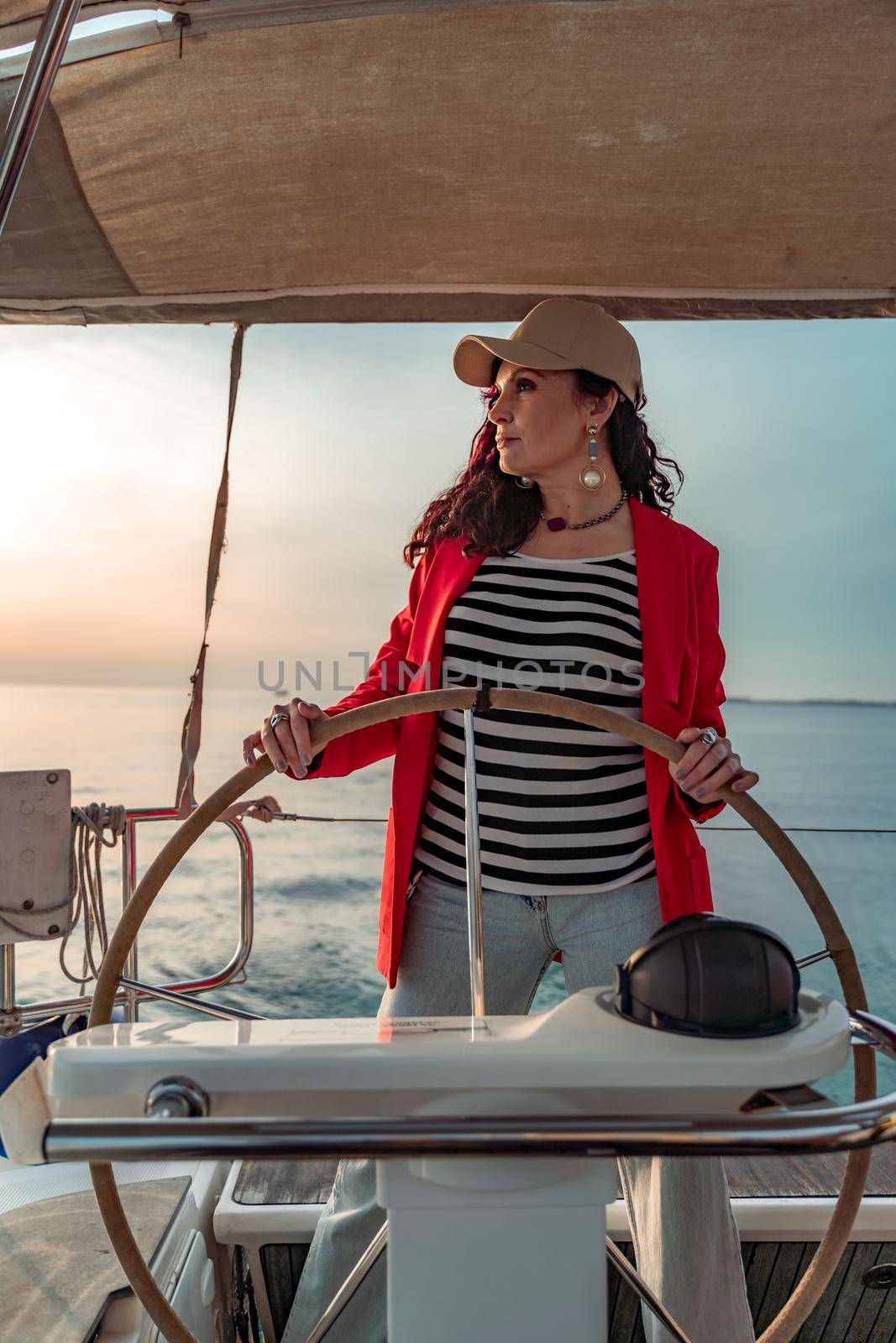 Attractive middle-aged woman at the helm of a yacht on a summer day. Luxury summer adventure, outdoor activities