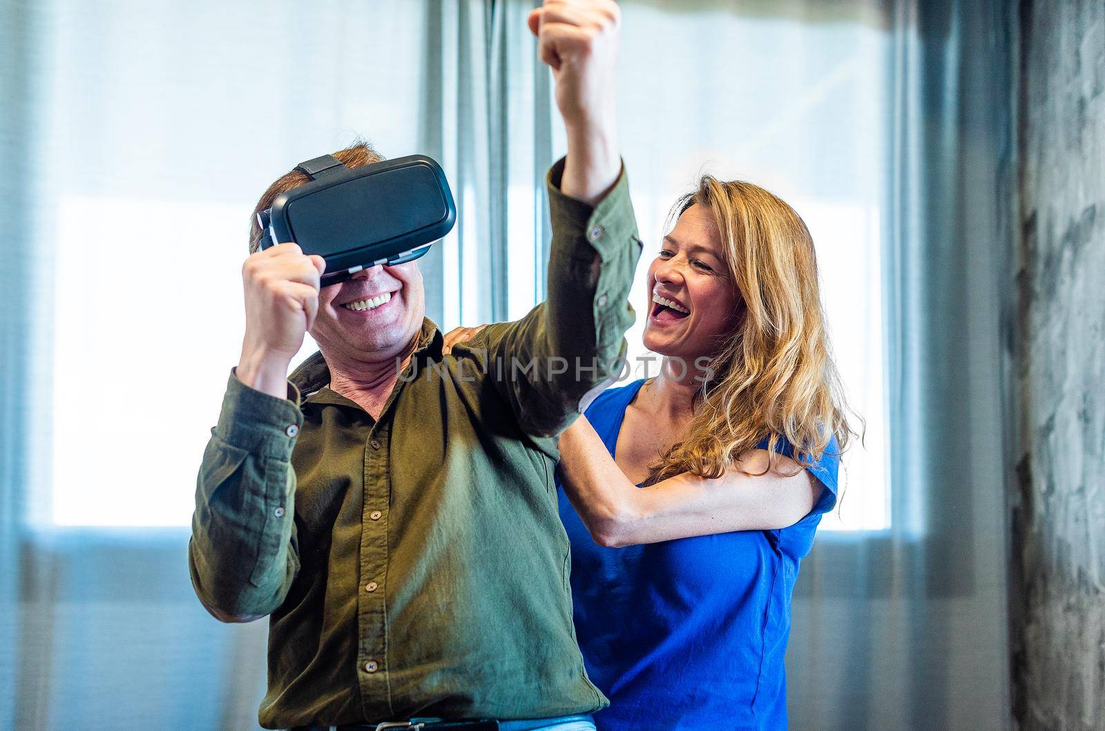 Mature married couple at home playing with virtual reality glasses. by ivanmoreno