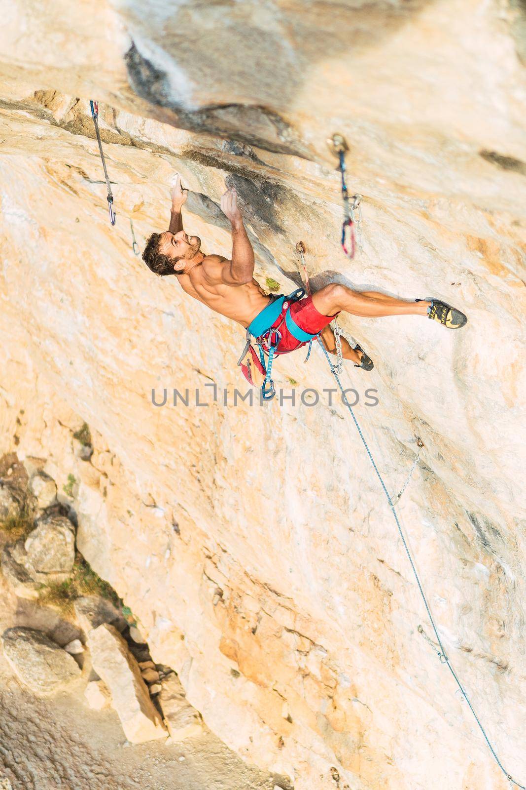 Rock climber holding with both hands on rock. Climber with bare torso climbing a rock wall.