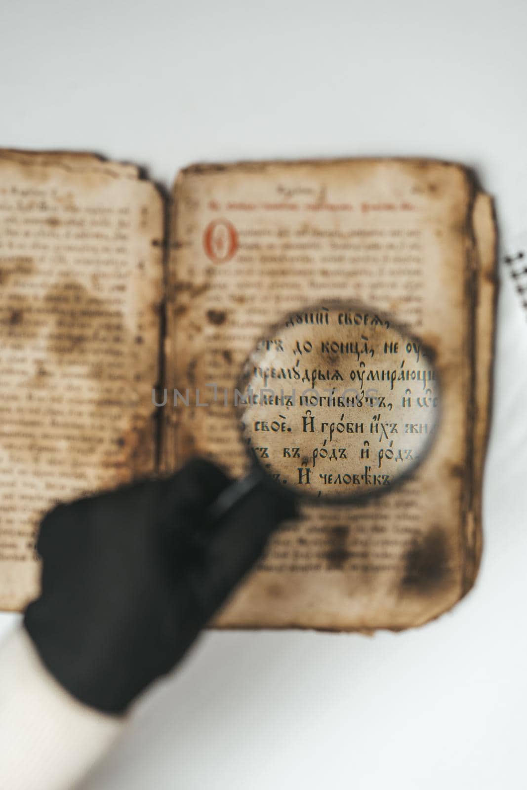 Historian scientist in gloves reading antique book with magnifying glass. Translation of religious literature. Manuscript with ancient writings. Treasures of the past. Museum piece. High quality