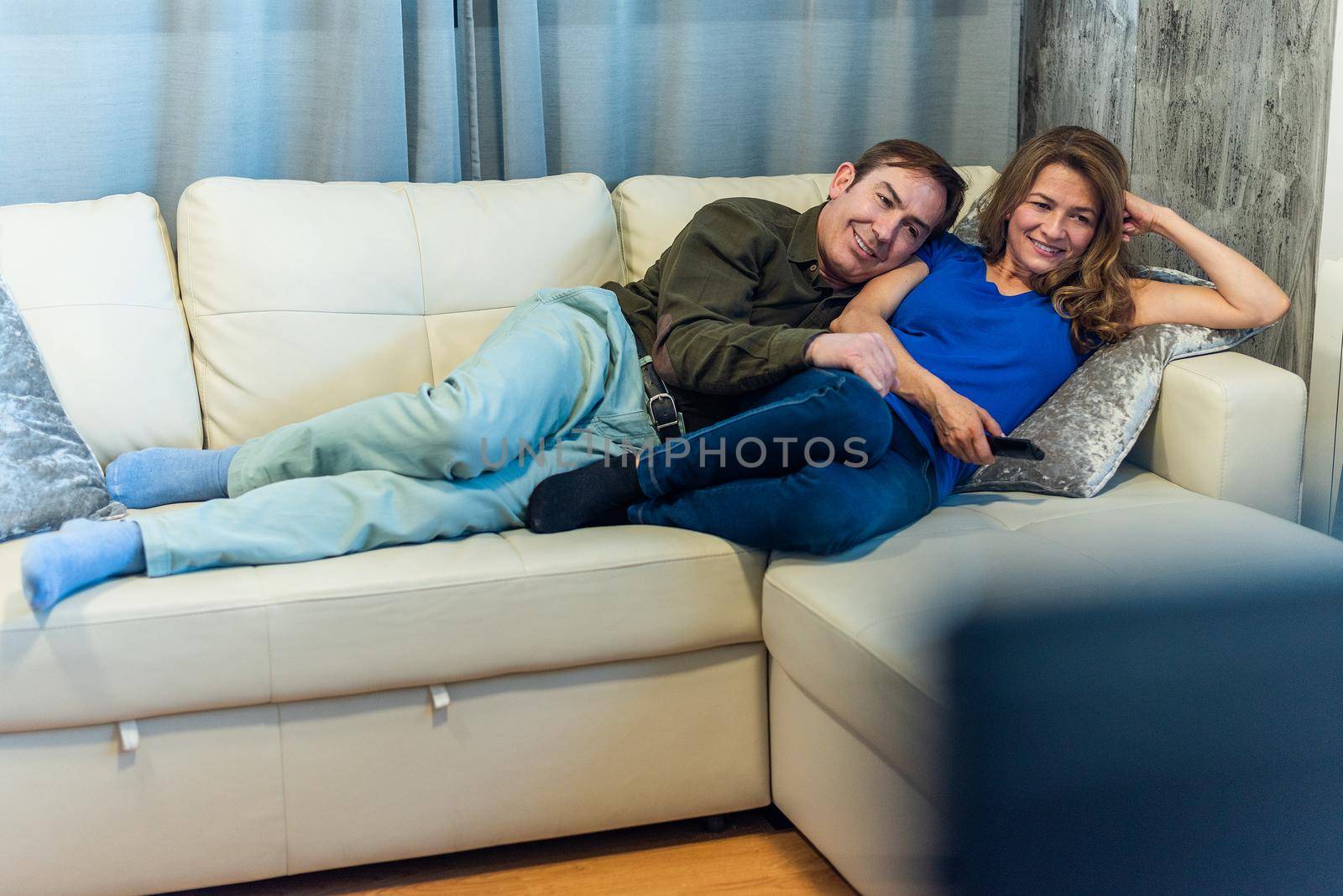 Mature man and woman lying on the couch watching a movie. High quality photo