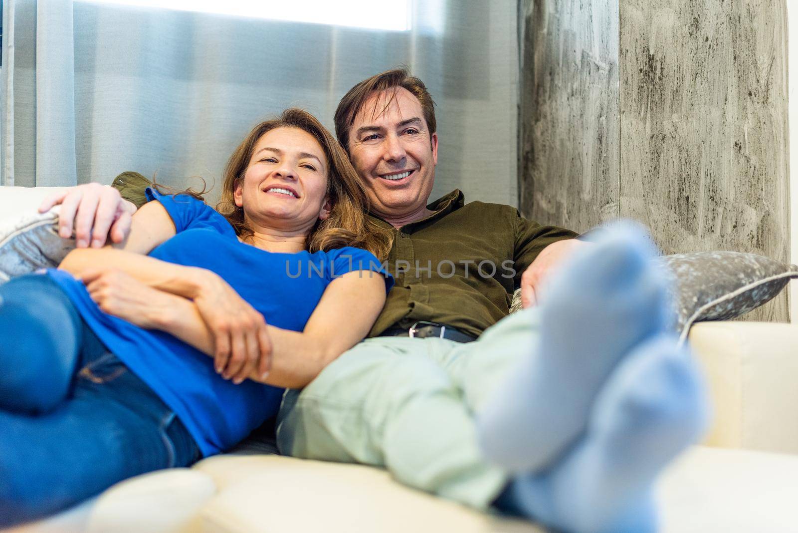 Mature man and woman lying on the couch watching TV. High quality photo