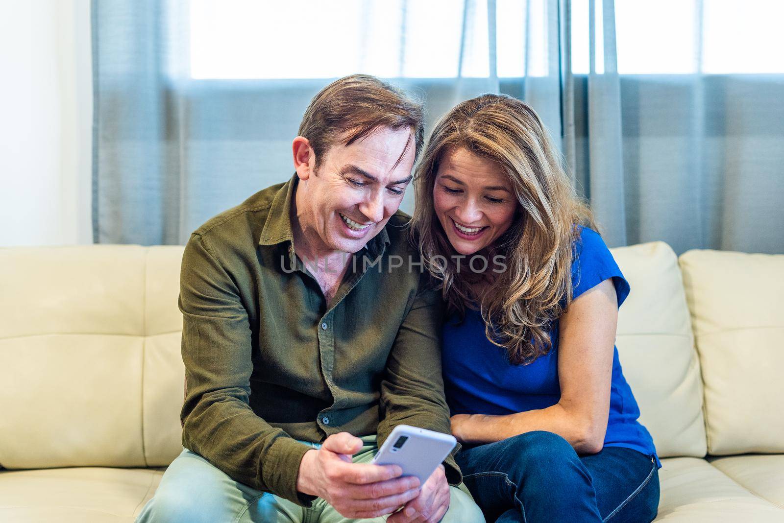 Smiling mature couple at home watching something funny on mobile. High quality photo